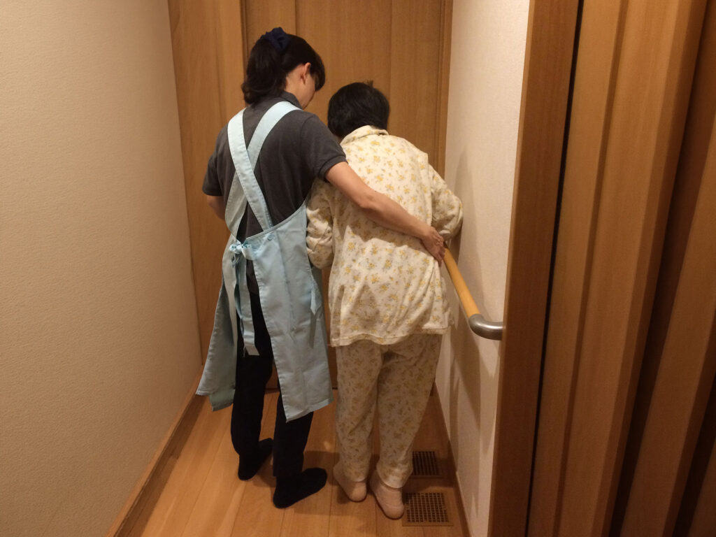 家の中で高齢者の歩行を支えるスタッフ